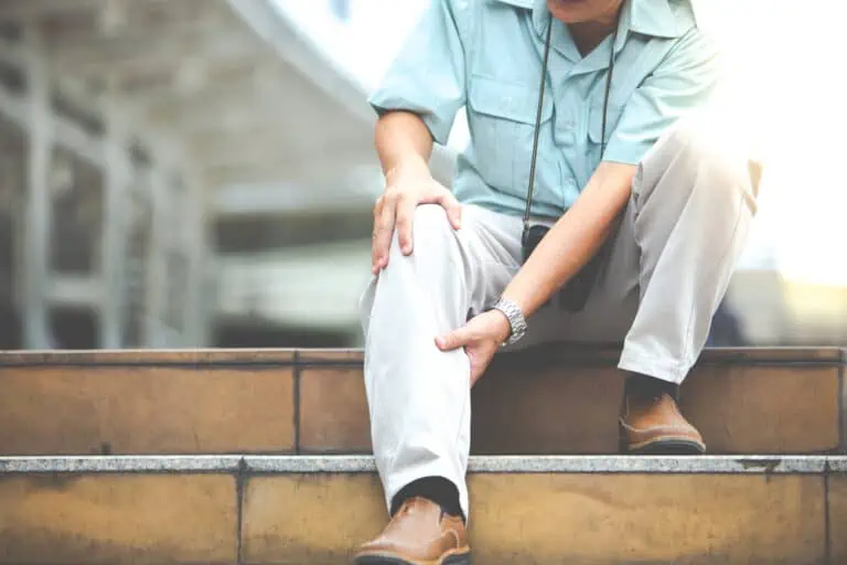 Man sits on steps, clutching his calf and knee